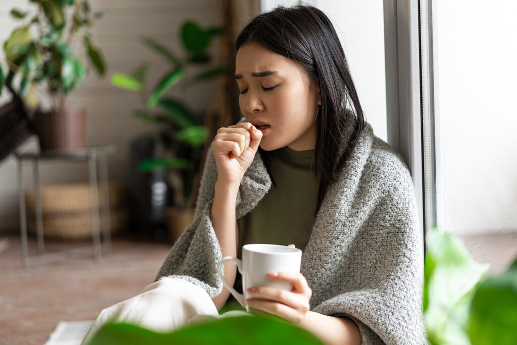 Cô gái trẻ mệt mỏi, có thể bị bệnh, ngồi gần cửa sổ, biểu hiện sức khỏe suy giảm